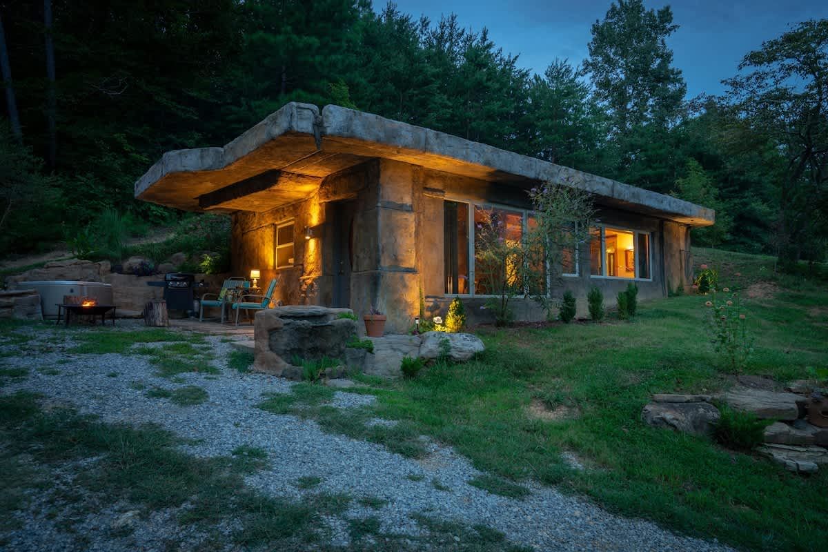 The stone cottage lit up at dusk, with the fire pit out front