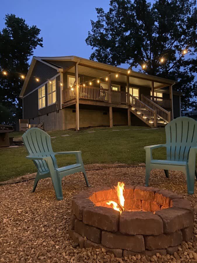 The house at dusk, string lights on the porch and chairs around the fire pit