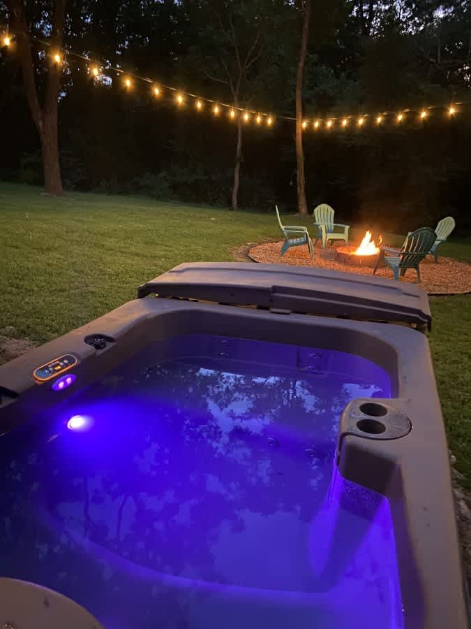 Hot tub lit purple at night beside the fire pit